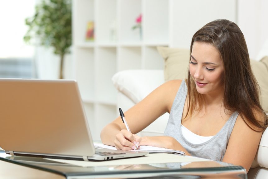Smiling young woman taking notes from online classes in front of a laptop