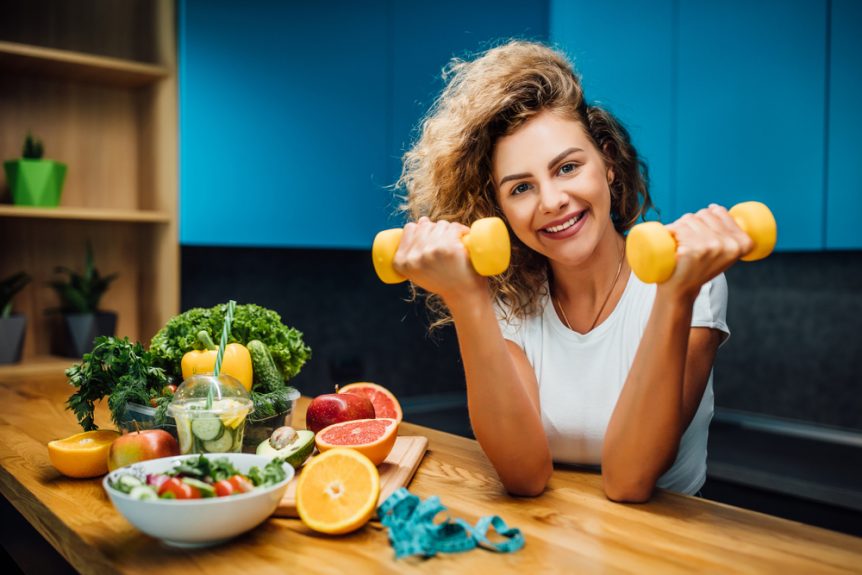 Personal trainer holding small weights surrounded by nutritious foods