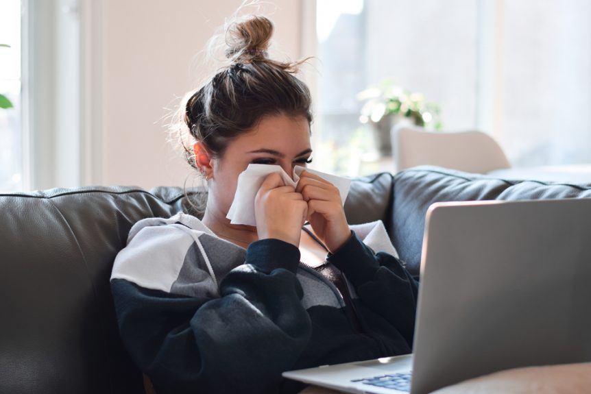 Young woman studying for online classes at home blowing nose with tissue