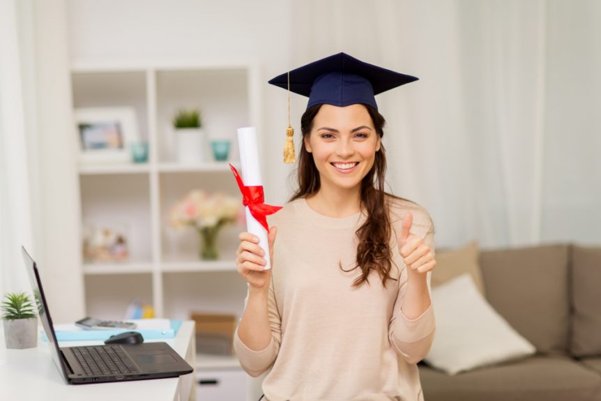 Young Woman Wearing a Cap Holding a Diploma Near a Laptop