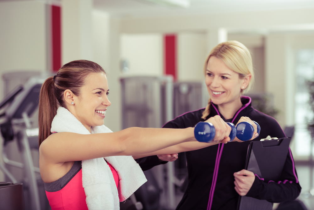 Smiling woman using handweights with a personal trainer looking on