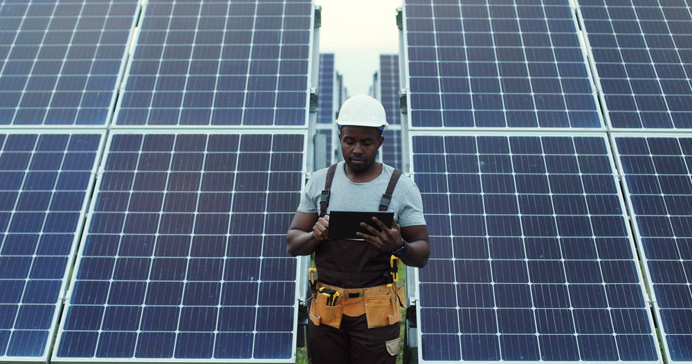 Solar Energy Technician Standing between two solar panels holding a tablet computer